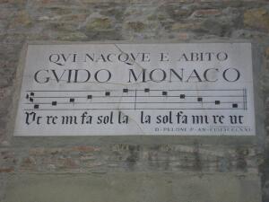Мемориальная доска в Ареццо на улице Рикасолли на доме, в котором родился Гвидо.  На ней изображены квадратные ноты.