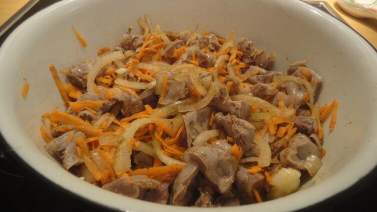 Добавляем к желудкам пошинкованную полукольцами луковицу и тертый на крупной терке корнеплод моркови, перемешиваем