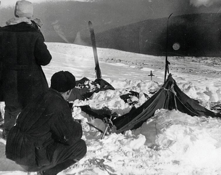 Палатка группы Дятлова, частично раскопанная от снега. Фото участника поисков А. С. Чеглакова (по другим сведениям, В. Д. Брусницына). Слева от палатки поисковики: Ю. Коптелов, за ним В. Карелин
